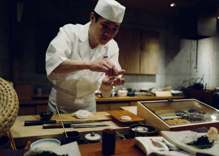 A chef serving up Japanese sushi, handing sushi to a waiting guest.